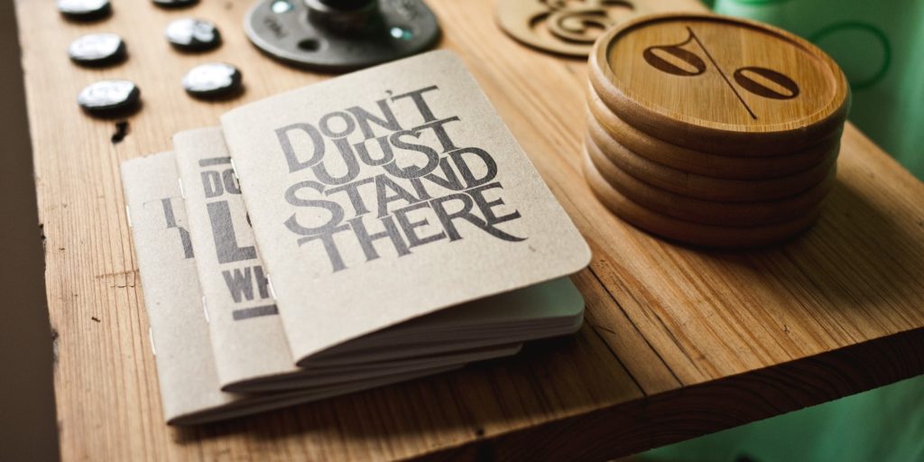 pile of notebooks on a desk, the topmost reading 'don't just stand there'