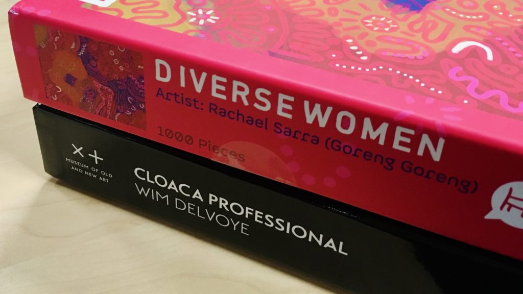 Two puzzle boxes stacked on top of each other: Rachael Sarra's Diverse Women and Wim Delvoye's Cloaca jigsaw puzzle