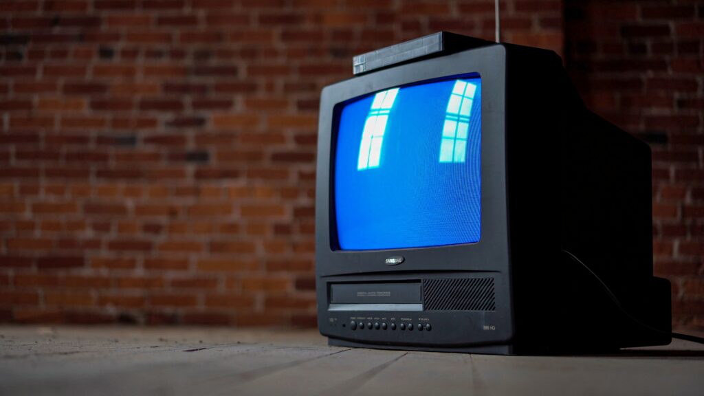An old 90s television displaying a blue screen, set in front of a red brick wall